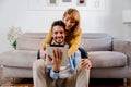 Happy couple of millennials using digital tablet at home. Boyfriend and girlfriend sitting on the sofa