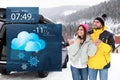 Couple near car on snowy road and weather forecast widget. Mobile application