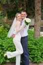 Happy couple newlyweds in the park. The bride wears trousers and a veil.