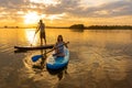 Happy couple paddle boarding at lake during sunset together with pug dog. active family tourism