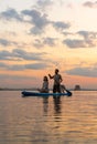 Happy couple paddle boarding at lake during sunset together with pug dog. active family tourism