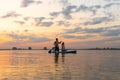 Happy couple paddle boarding at lake during sunset together with pug dog. active family tourism