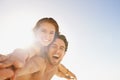 Happy couple, portrait and piggyback in support with blue sky at beach in love, care or enjoying outdoor holiday weekend Royalty Free Stock Photo