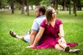 Happy couple resting in a park on green grass. Slow motion. Smiling man and woman talking while enjoying a warm summer Royalty Free Stock Photo