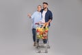 Happy couple with shopping cart full of groceries on light grey background Royalty Free Stock Photo