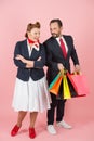 Happy couple at shopping time. Man holds lot of colored bags with presents for woman. pin-up styled couple on rose background Royalty Free Stock Photo