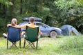 Happy couple sitting on chairs at campsite hugging together. Travel, camping and vacations concept