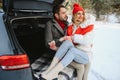 Happy couple sitting in open car back, having stop off. Romantic traveling concept. Winter forest Royalty Free Stock Photo