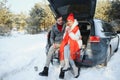 Happy couple sitting in open car back, having stop off. Romantic traveling concept. Winter forest Royalty Free Stock Photo