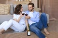 Happy couple sitting, relaxing on floor in living room, drinking red wine. Smiling young husband and wife rest at home Royalty Free Stock Photo