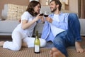 Happy couple sitting, relaxing on floor in living room, drinking red wine. Smiling young husband and wife rest at home Royalty Free Stock Photo