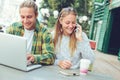 Happy couple sitting in street cafe, woman talking on the phone and man using laptop Royalty Free Stock Photo