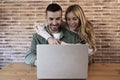 Happy couple sitting and working together from home with a laptop. Young adult man and woman using computer online in Royalty Free Stock Photo