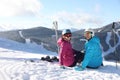 Happy couple with ski equipment sitting on hill in mountains, space for text. Winter vacation Royalty Free Stock Photo
