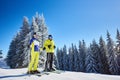 Happy couple skiers posing on skis before skiing at ski resort. Clear blue sky, snow-covered fir trees on background.