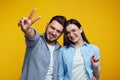 Happy couple smiling and showing peace gesture over yellow background Royalty Free Stock Photo