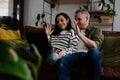 Happy couple smiling and waving while on video call with overseas family using laptop sitting on sofa in lounge. Royalty Free Stock Photo