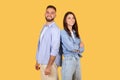 Happy couple standing back-to-back with confident smiles on yellow background