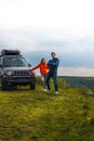 Happy couple standing on the top of the mountain. Car trip on SUV with roof rack, trip at warm summer day. Man and woman enjoying Royalty Free Stock Photo