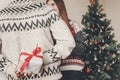 happy couple in stylish sweaters exchanging gifts in festive room at christmas tree. man holding surprise present behind back. me Royalty Free Stock Photo