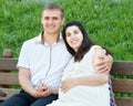 Happy couple in summer city park outdoor, pregnant woman, bright sunny day and green grass, beautiful people portrait Royalty Free Stock Photo