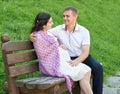 Happy couple in summer city park outdoor, pregnant woman, bright sunny day and green grass, beautiful people portrait Royalty Free Stock Photo