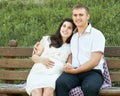 Happy couple in summer city park outdoor, pregnant woman, bright sunny day and green grass, beautiful people portrait, yellow tone Royalty Free Stock Photo