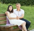 Happy couple in summer city park outdoor, pregnant woman, bright sunny day and green grass, beautiful people portrait, yellow tone Royalty Free Stock Photo