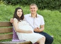 Happy couple in summer city park outdoor, pregnant woman, bright sunny day and green grass, beautiful people portrait, yellow tone Royalty Free Stock Photo