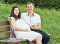 Happy couple in summer city park outdoor, pregnant woman, bright sunny day and green grass, beautiful people portrait, yellow tone Royalty Free Stock Photo