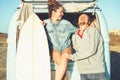 Happy couple of surfers standing behind on vintage camper van - Young people adventuring on road trip with a minivan transport Royalty Free Stock Photo