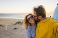 Happy couple take selfie picture at the beach with love and kiss - concept of people tourists enjoy the outdoor leisure activity