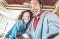 Happy couple taking a selfie in mini van camper during a roadtrip - Travel people having fun making pictures with mobile phone