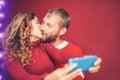 Happy couple taking selfie with mobile smartphone camera - Young romantic lovers kissing and celebrating Christmas holidays Royalty Free Stock Photo