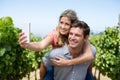 Happy couple taking selfie while piggybacking at vineyard against sky Royalty Free Stock Photo