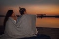 Happy couple of teens enjoying in romantic date while sitting covered with blanket during sunset Royalty Free Stock Photo