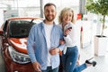 Happy couple and their new car in dealership. Royalty Free Stock Photo