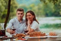 Happy couple toasting red wine glass while having picnic french dinner party outdoor during summer holiday vacation near Royalty Free Stock Photo