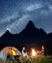 Happy couple tourists sitting near campfire and tent under incredibly beautiful starry sky at night. Long exposure Royalty Free Stock Photo