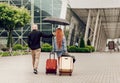 Happy couple traveling. Rear view, woman holding two suitcases, man holding umbrella, rainy day Royalty Free Stock Photo