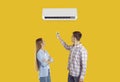 Happy couple use remote to set temperature on air conditioner isolated on yellow background Royalty Free Stock Photo