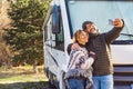 Happy couple of vanlife camper van tourist taking selfie picture with smartphone outside the travel vehicle home. Concept of