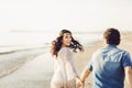 Happy couple walking along the sea, holding hands. The girl has a flower wreath on her head. Love story. Back view Royalty Free Stock Photo