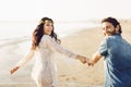 Happy couple walking along the sea, holding hands. The girl has a flower wreath on her head. Love story. Back view Royalty Free Stock Photo