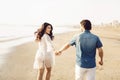 Happy couple walking along the sea, holding hands. Girl in white dress, man in a jeans shirt. Love story. Back view Royalty Free Stock Photo