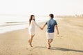 Happy couple walking along the sea, holding hands. Girl in white dress, man in a jeans shirt. Love story. Back view Royalty Free Stock Photo