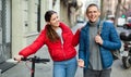 Couple are walking along the spring street. Girl with electric scooter Royalty Free Stock Photo