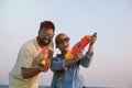 Happy couple with water guns against light blue sky at sunset