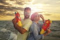 Happy couple with water guns near sea at sunset