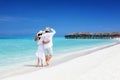Happy couple in white clothing and with hats walks down a tropical beach Royalty Free Stock Photo